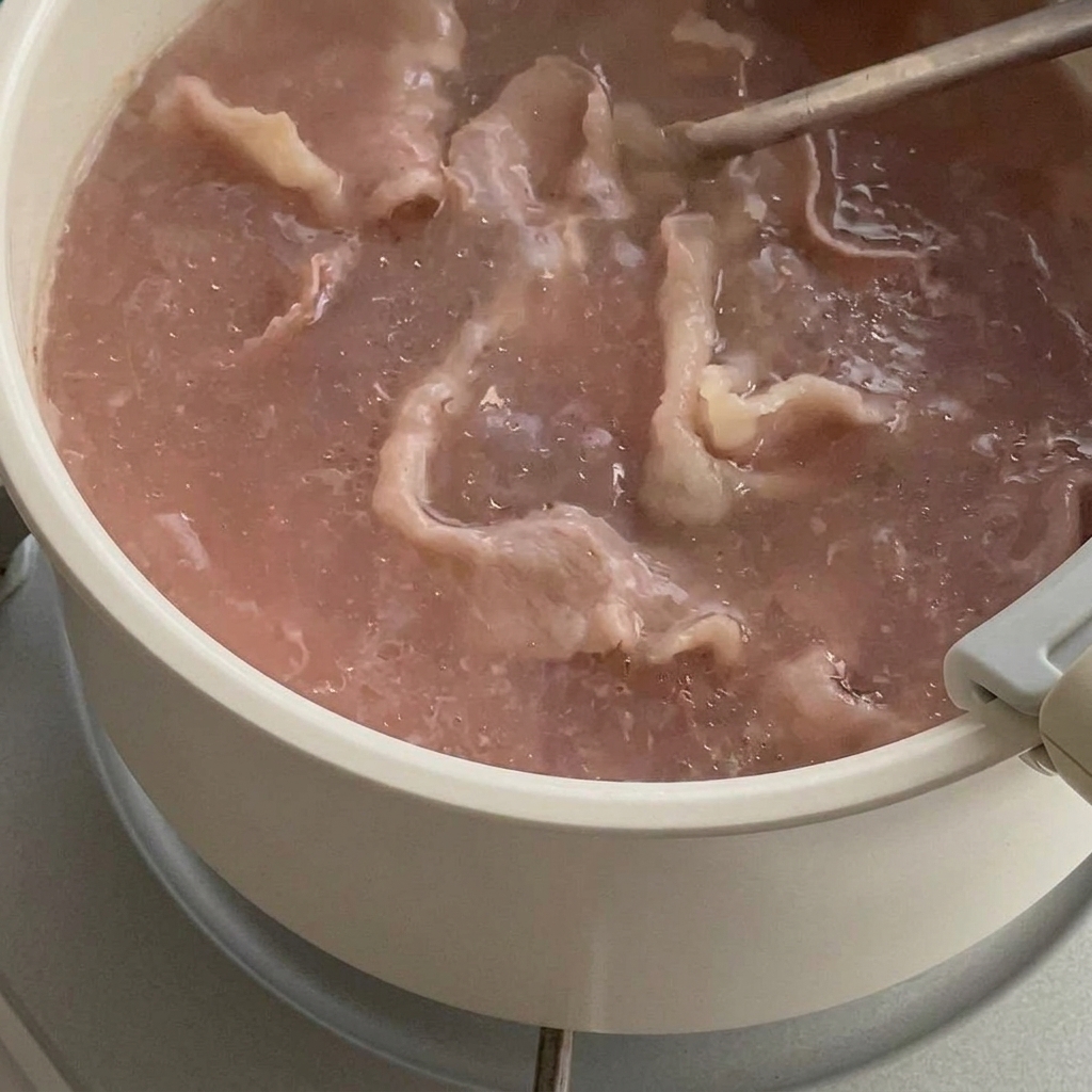 Tranches de bœuf partiellement cuites dans une casserole deau, soulevées avec une écumoire.