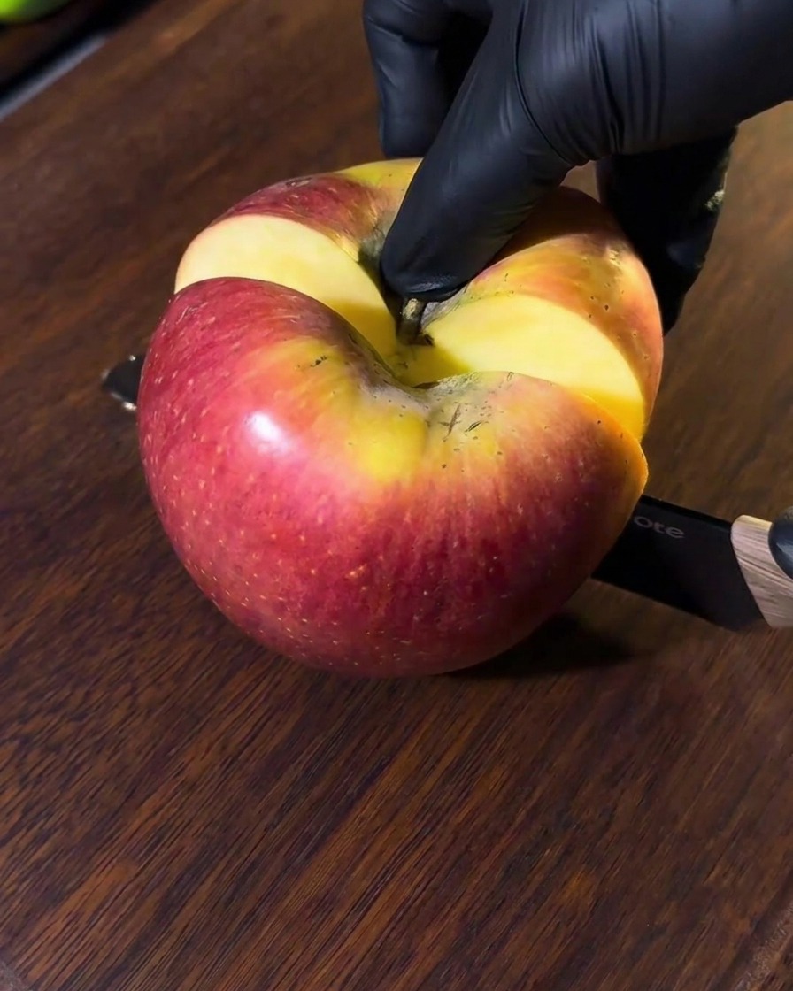 Une pomme en train dêtre tranchée sur une planche à découper en bois, avec des morceaux prêts à être mixés.