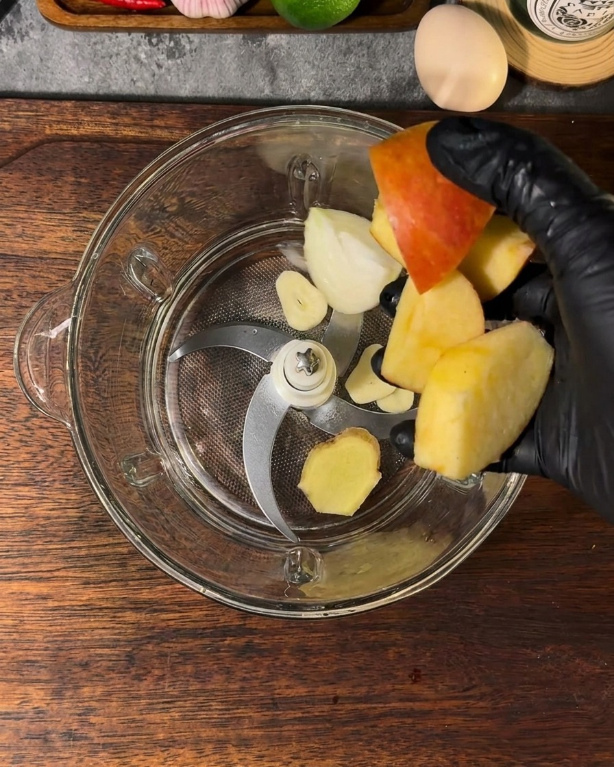 Un bol de mixeur rempli de morceaux de pomme, de segments doignon, dail, de gingembre et deau.