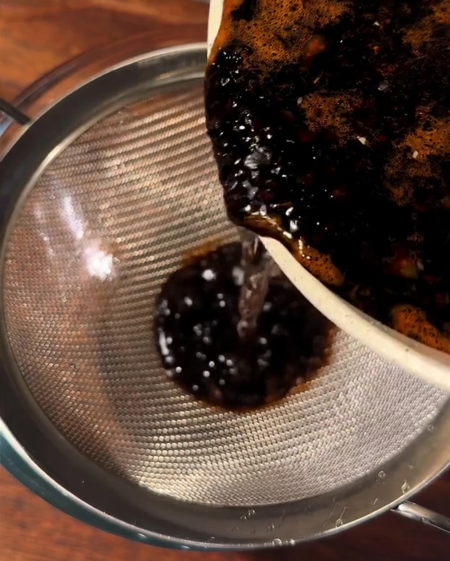 Sauce brun foncé versée à travers une passoire métallique dans un bol en verre.