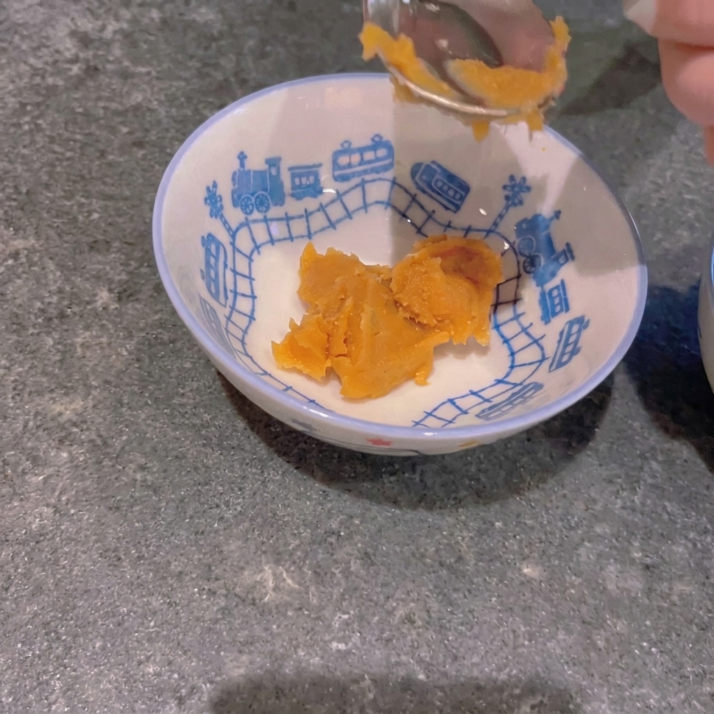 Une cuillère de pâte de miso jaune placée dans un petit bol à motif de train.