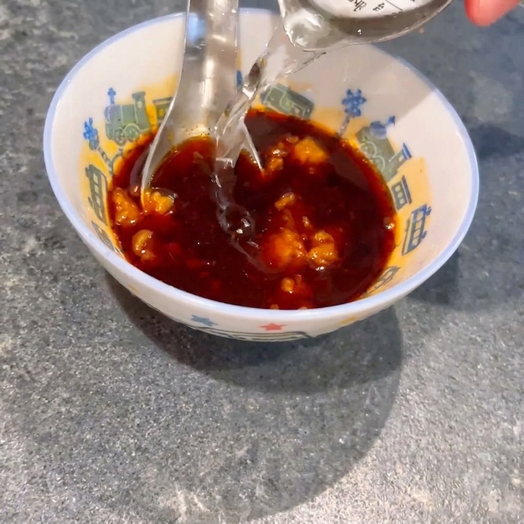 De leau versée dans un petit bol contenant de la sauce soja et des morceaux de miso, remuée avec une cuillère.