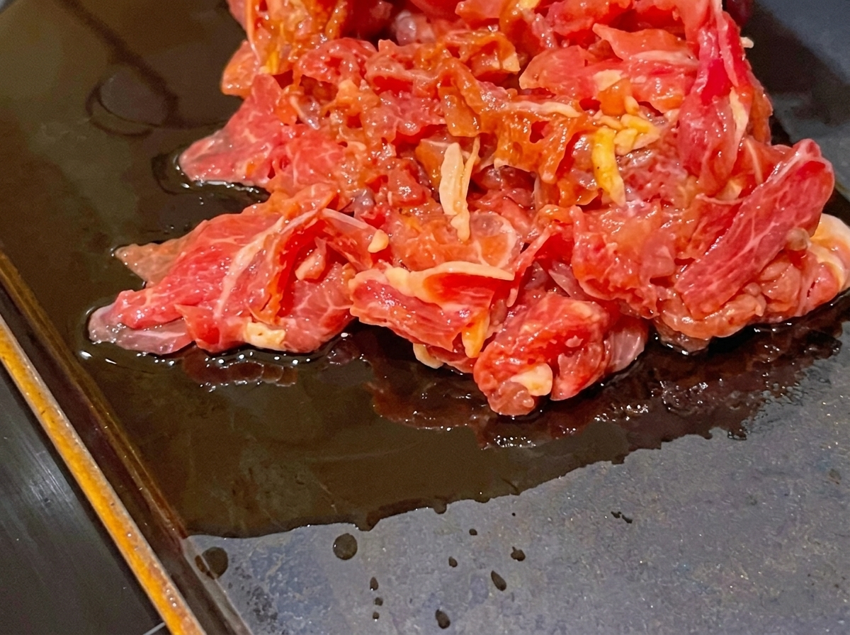 Un tas de tranches de bœuf cru mariné sur une poêle chaude et plate.