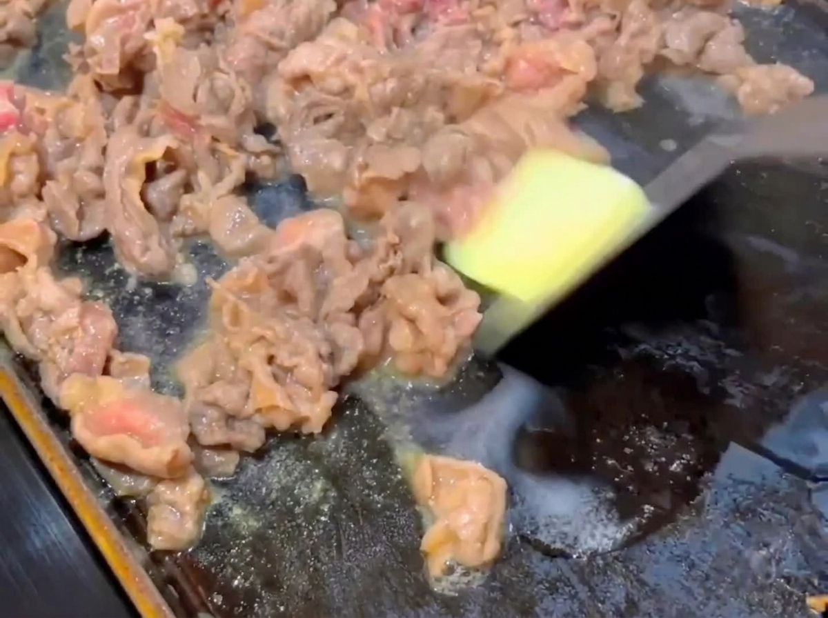 Une petite noisette de beurre fondant sur des tranches de bœuf partiellement cuites dans une poêle chaude.