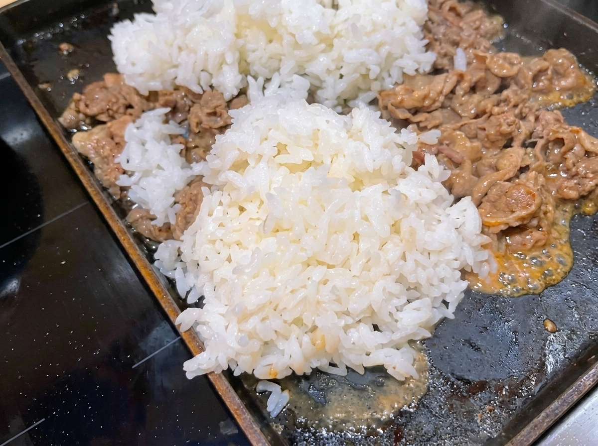 Une généreuse portion de riz blanc cuit ajoutée dans la poêle avec le bœuf en cours de cuisson.