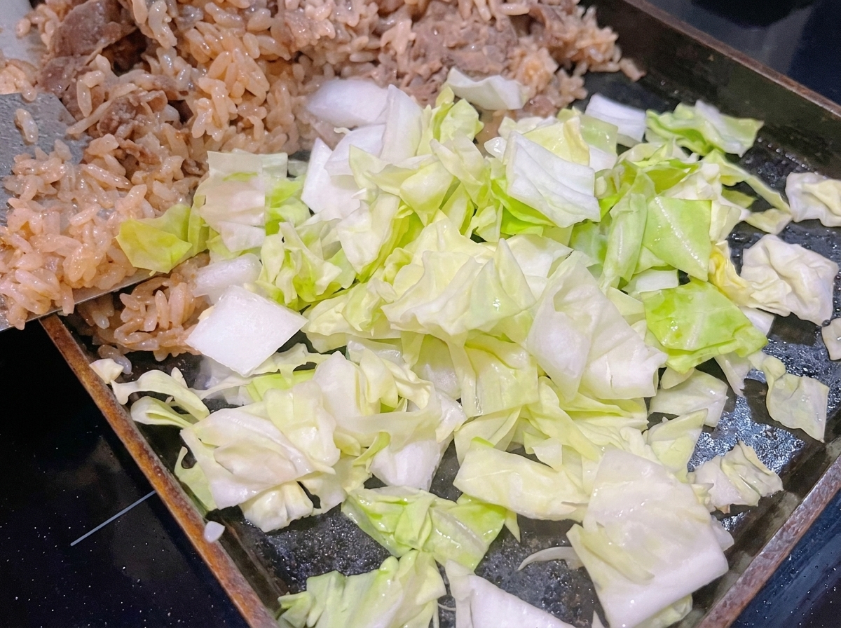 Chou vert frais émincé placé au-dessus du riz et du bœuf dans une poêle chaude.