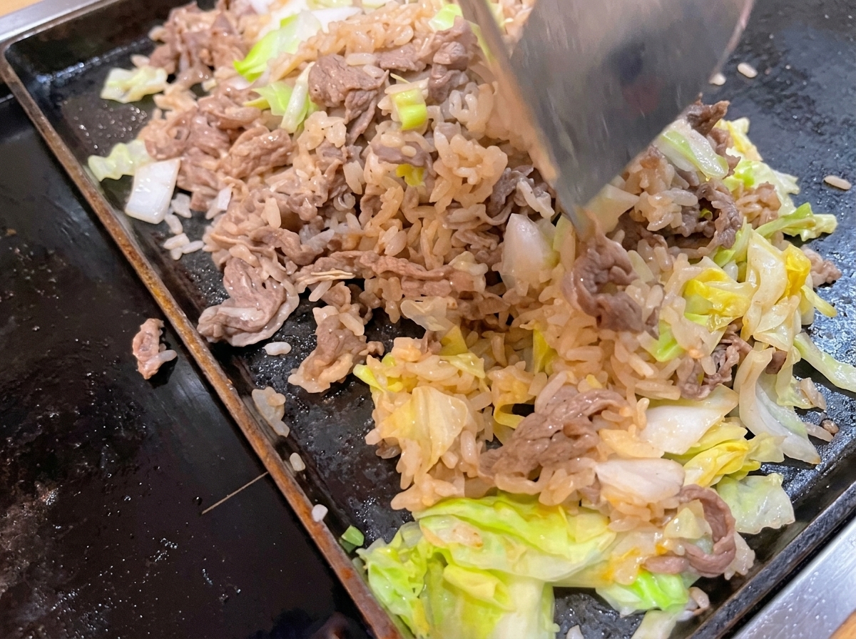 Une spatule en métal mélangeant le bœuf, le riz et le chou dans une poêle chaude.