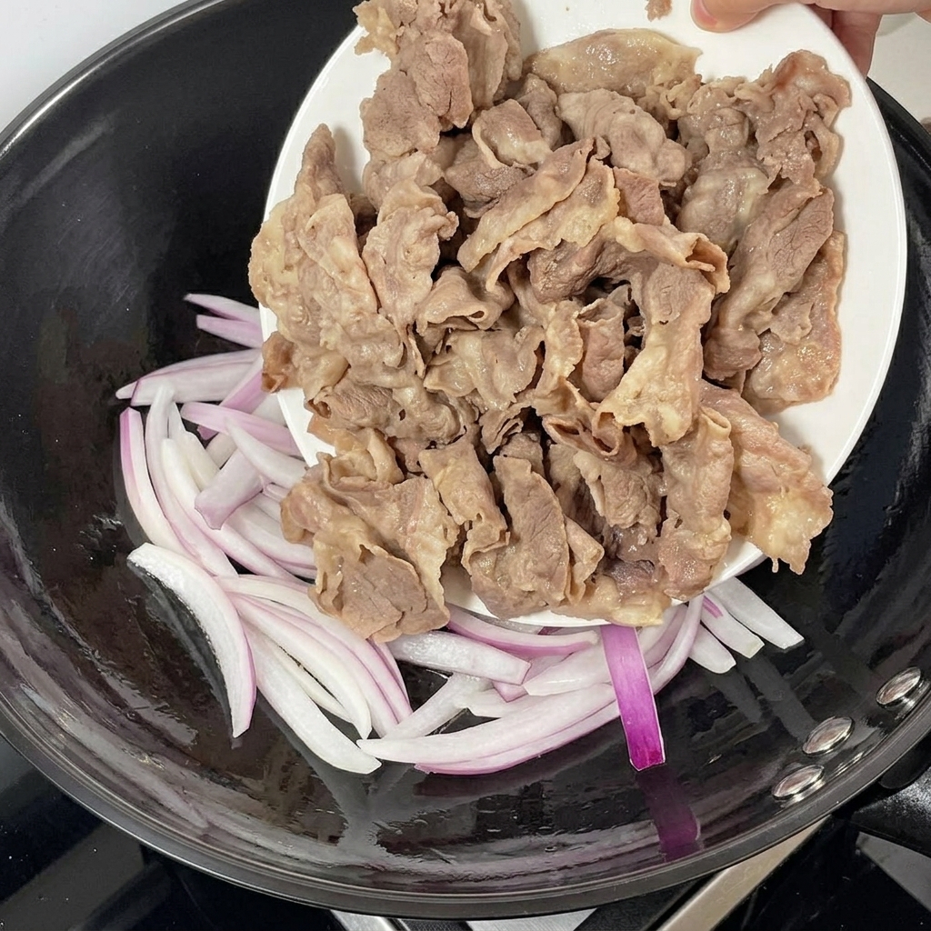 Bœuf blanchi ajouté dans une poêle avec des oignons rouges sautés.
