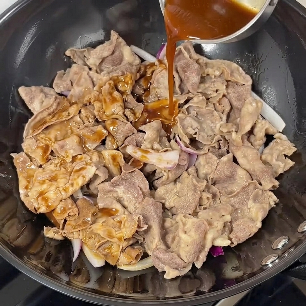 Sauce teriyaki foncée versée sur le bœuf et les oignons dans un wok.