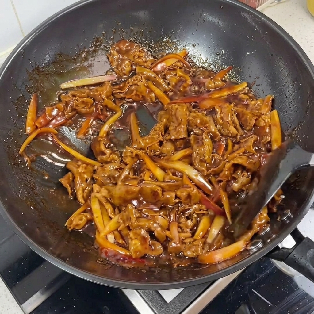 Gros plan sur des tranches de bœuf et des lamelles doignon rouge glacées dans une sauce teriyaki brillante dans un wok.