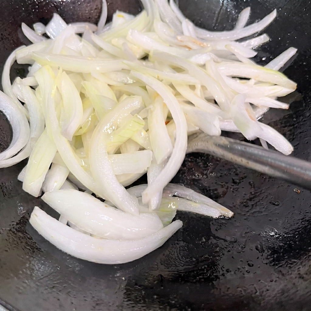 Oignons émincés en train de sauter dans un wok chaud.