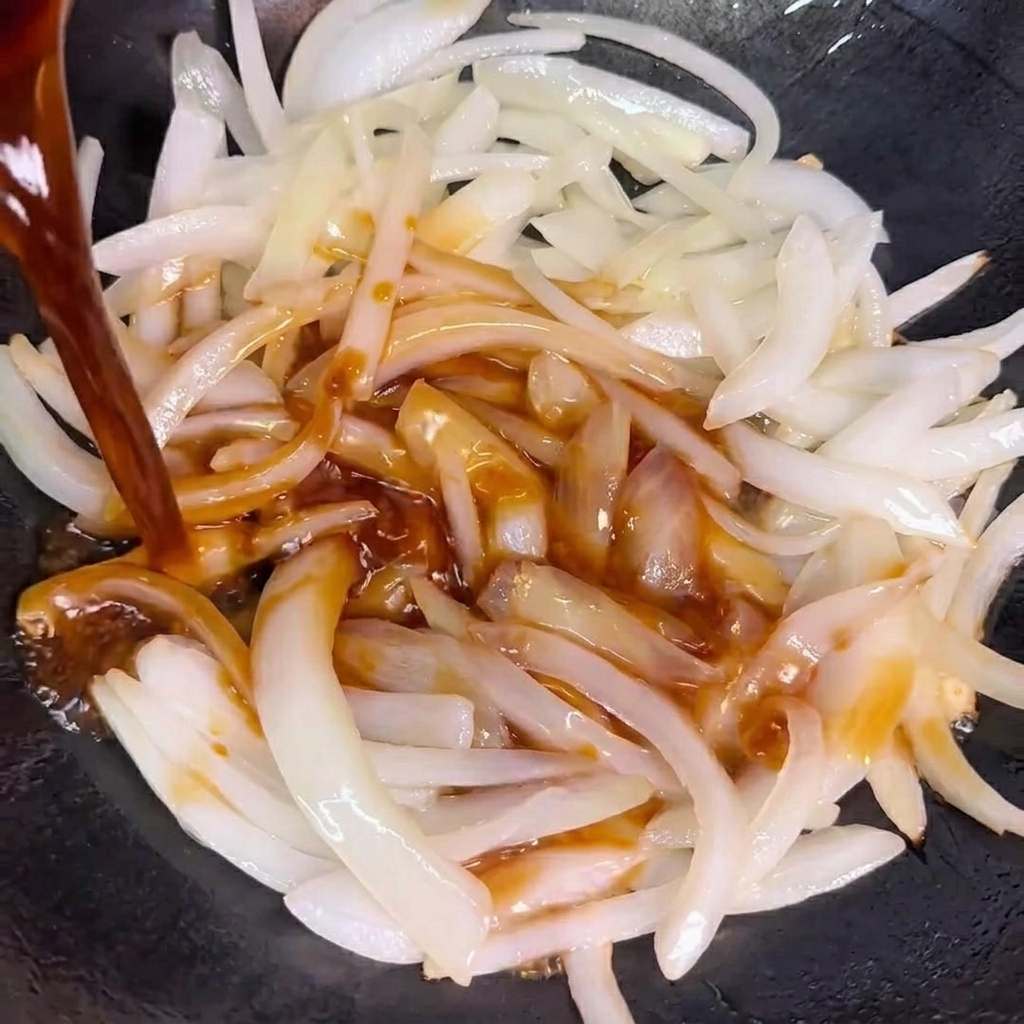 La sauce versée sur les oignons sautés dans un wok.