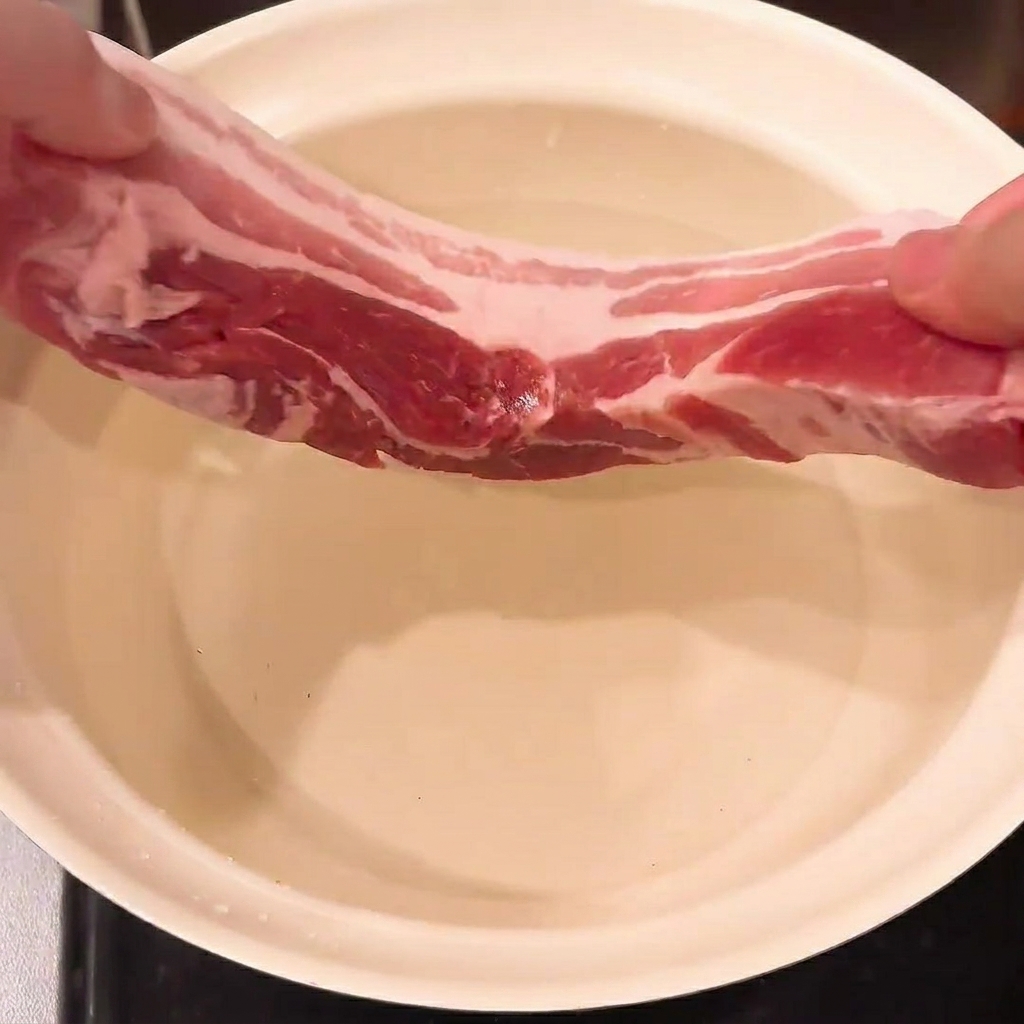 Poitrine de porc, oignon vert et gingembre immergés dans une casserole deau, prêts à blanchir.