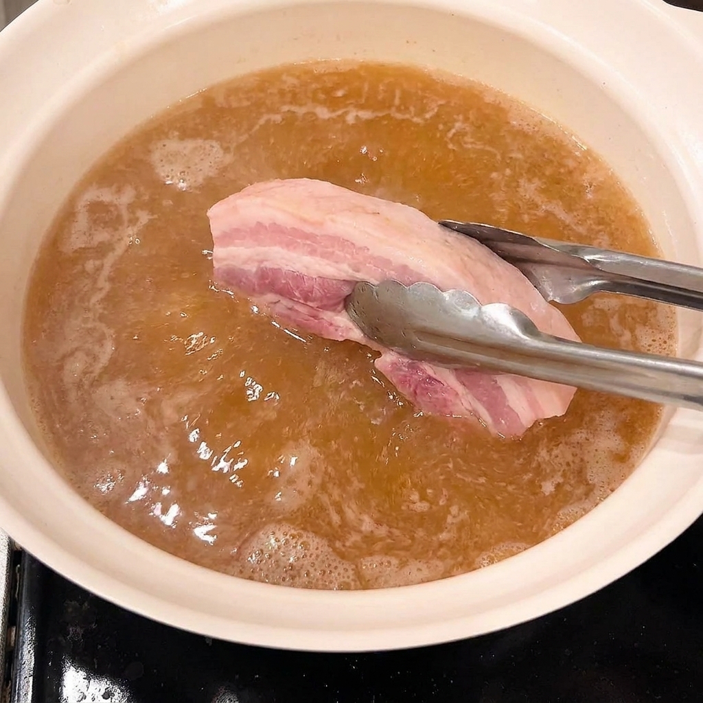 Pinces plaçant les morceaux de poitrine de porc blanchis dans une casserole de liquide de braisage frémissant.