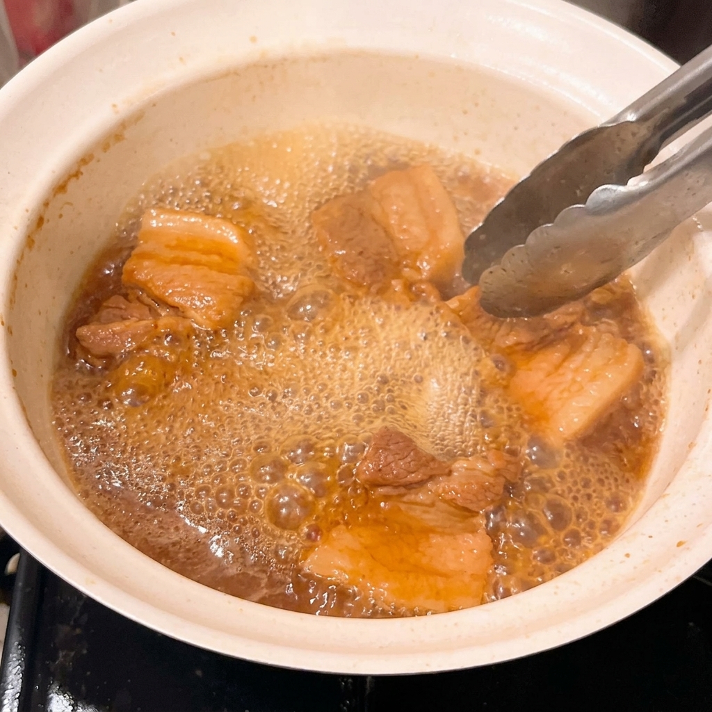 Gros plan sur les morceaux de porc tendres mijotant dans un glaçage au miso épaissi et bouillonnant.