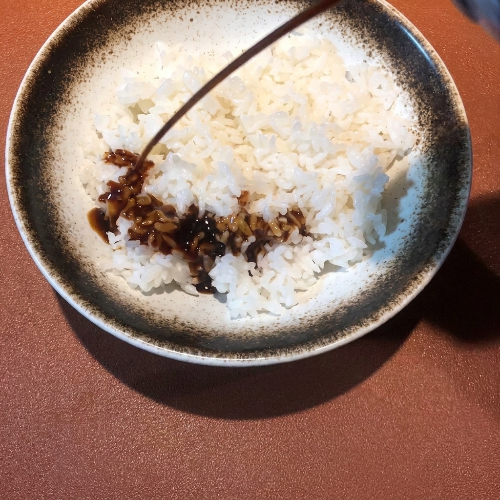 Sauce sombre versée sur un bol de riz blanc vapeur.