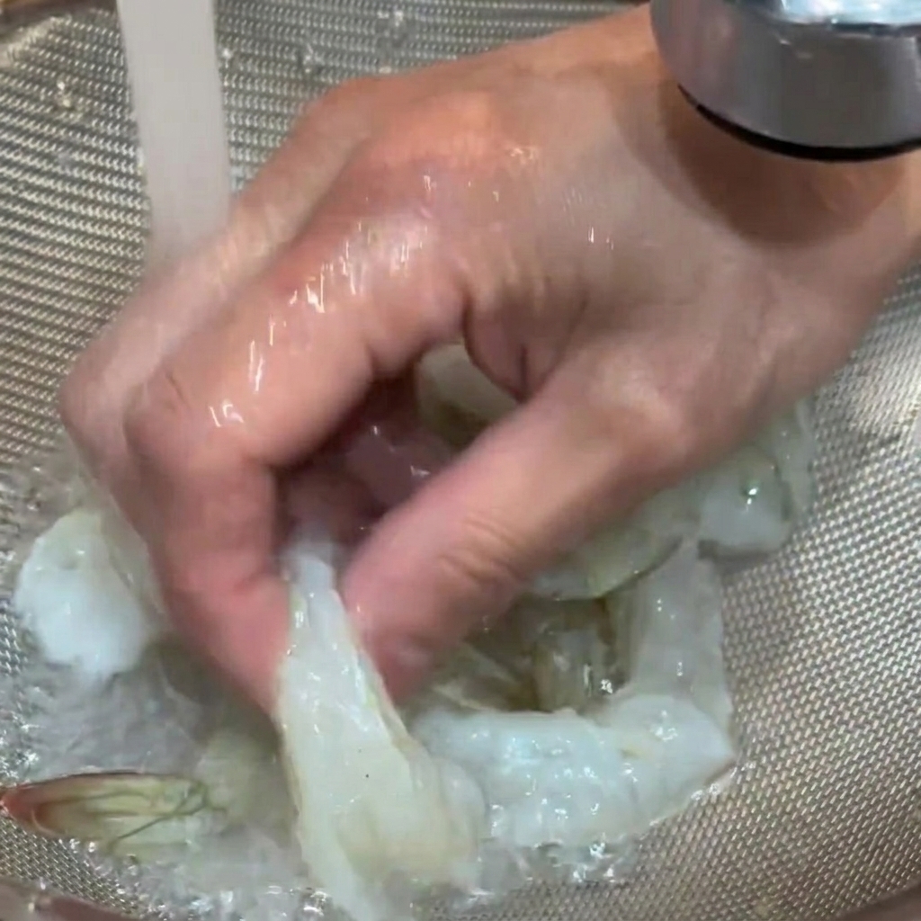Crevettes crues rincées à leau courante dans une passoire.