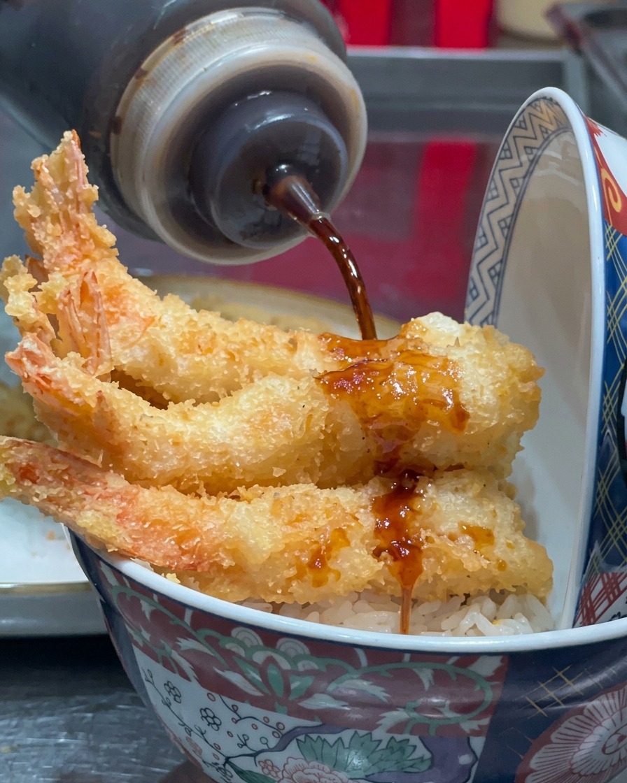 Sauce sombre versée depuis une bouteille souple sur les crevettes frites.