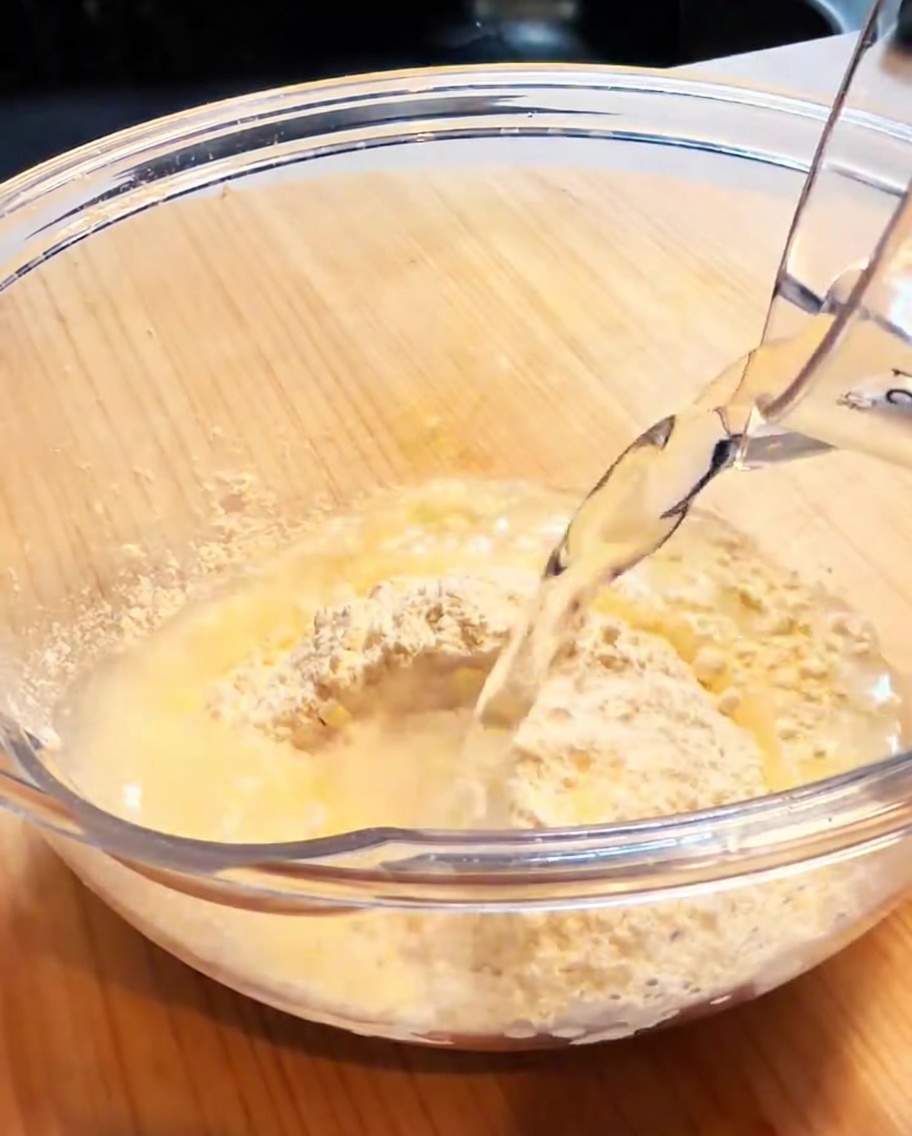 Un bol en verre contenant de la farine à tempura et de leau, en train dêtre fouetté pour former une pâte lisse et légère.