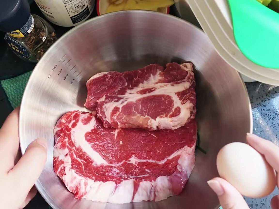 Un œuf cru cassé sur des côtes de porc fraîches dans un grand bol en inox.