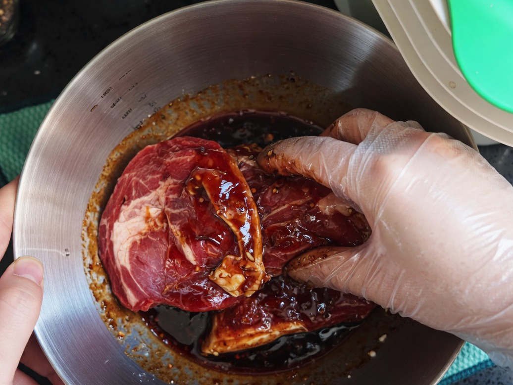 Une main munie dun gant mélangeant les côtes de porc crues avec la marinade.