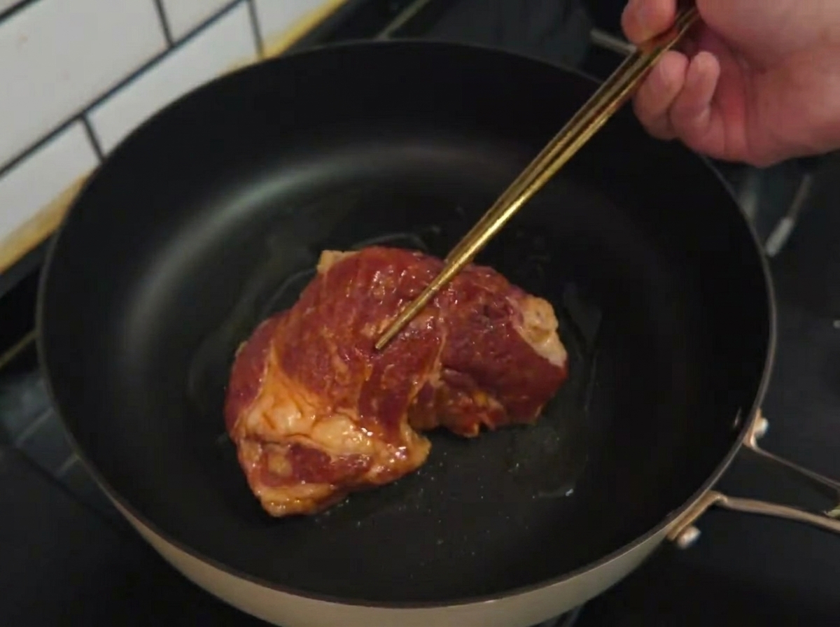 Une côte de porc marinée crue déposée dans une poêle chaude avec de lhuile.