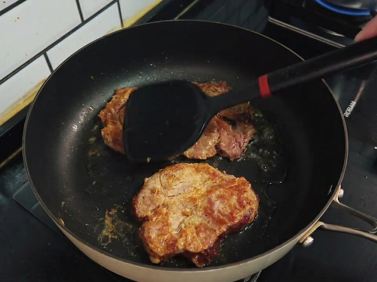 Une spatule retournant des côtes de porc dorées dans une poêle antiadhésive.