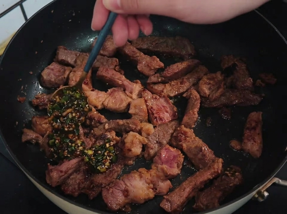 Une cuillère versant une sauce aromatique à la ciboule sur des lanières de porc dans la poêle.