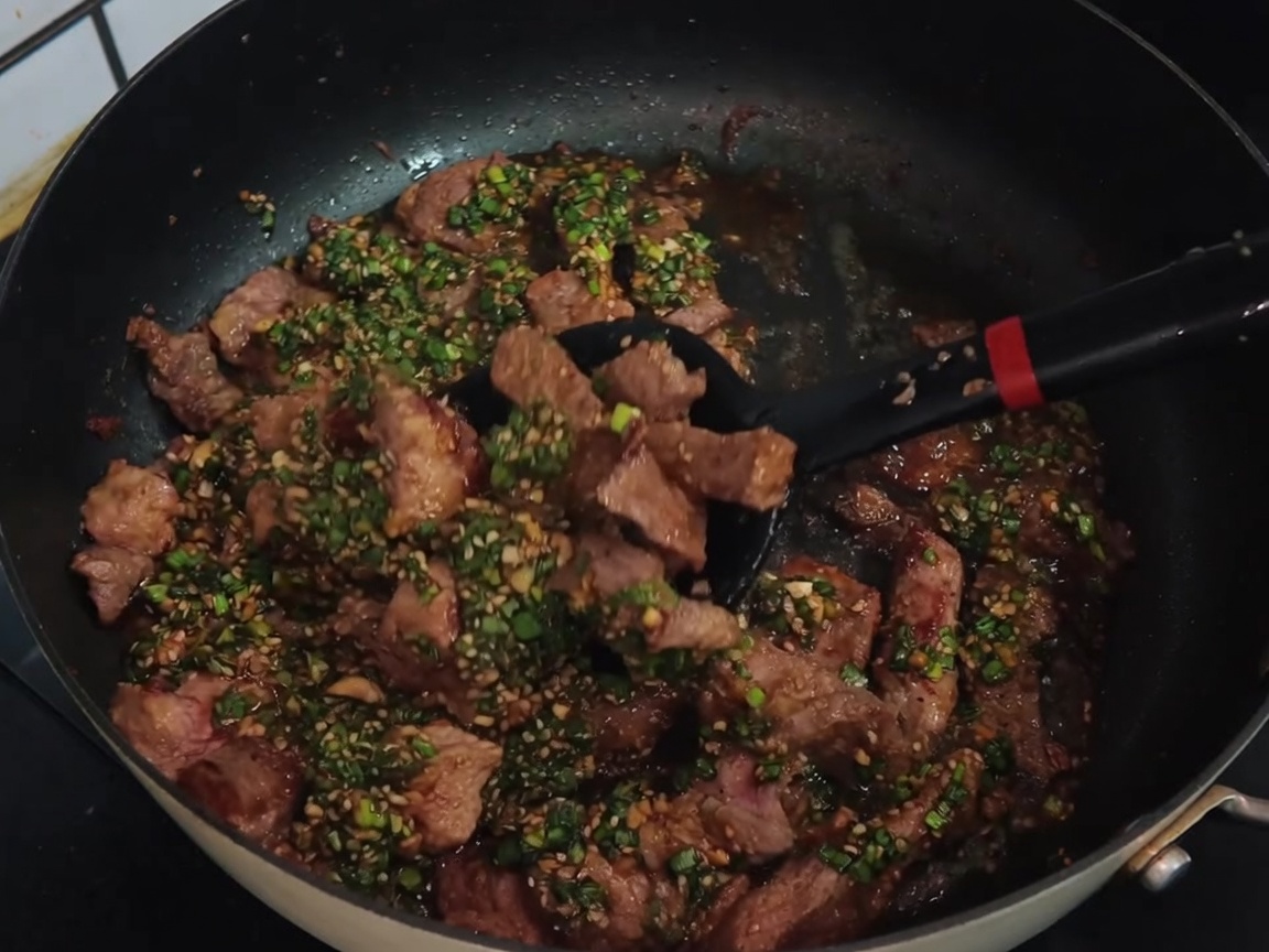 Une spatule noire mélangeant des tranches de porc avec une sauce verte dans une poêle.