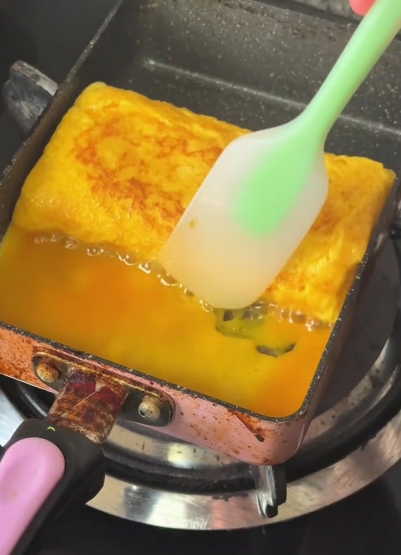 Une poêle rectangulaire avec une omelette dorée et multicouche pliée à laide dune spatule en silicone.