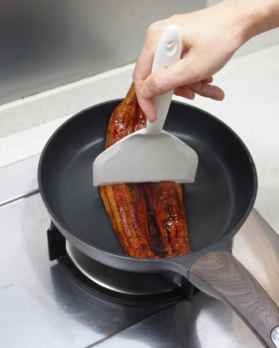 Languille grillée étant divisée en deux parts avec une spatule blanche dans la poêle.