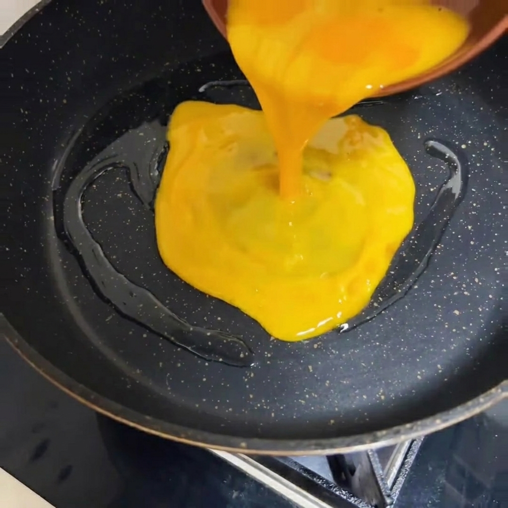 Le mélange dœufs battus étant versé dans une poêle chaude de couleur foncée.