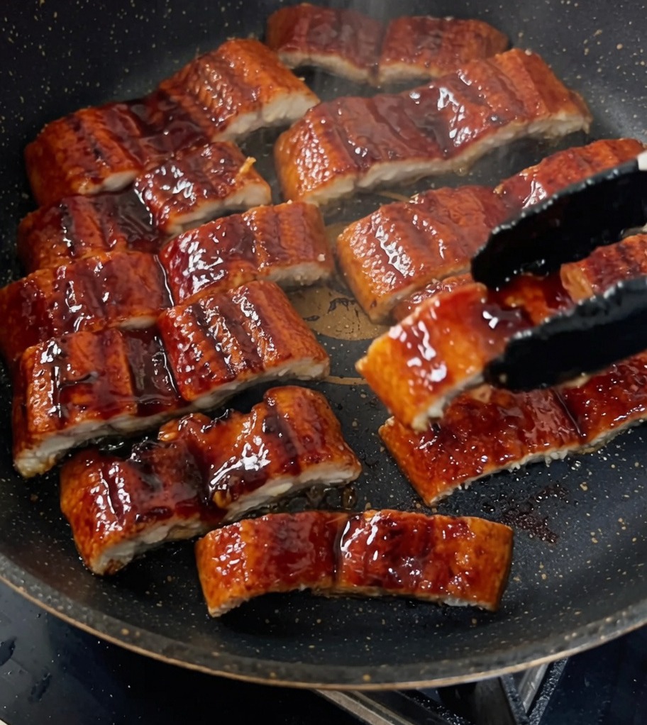 Des morceaux danguille grillée étant laqués dans une poêle avec une sauce riche et sombre.