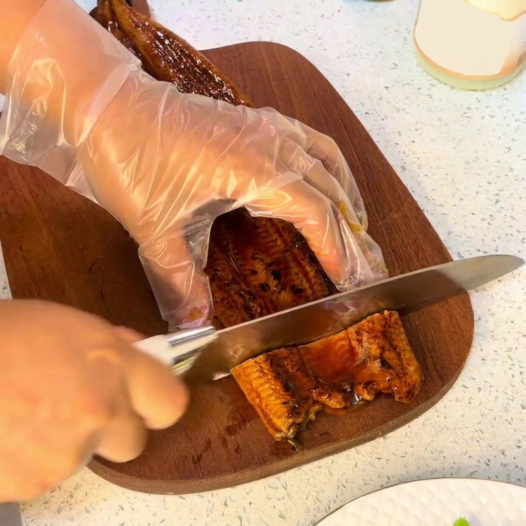 Un couteau coupant un morceau danguille grillée sur une planche à découper en bois.