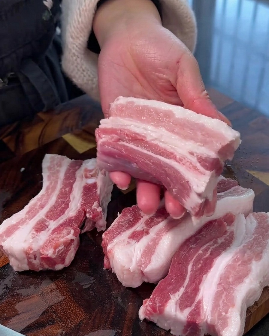 Poitrine de porc crue découpée en lanières épaisses et uniformes sur une planche à découper en bois.
