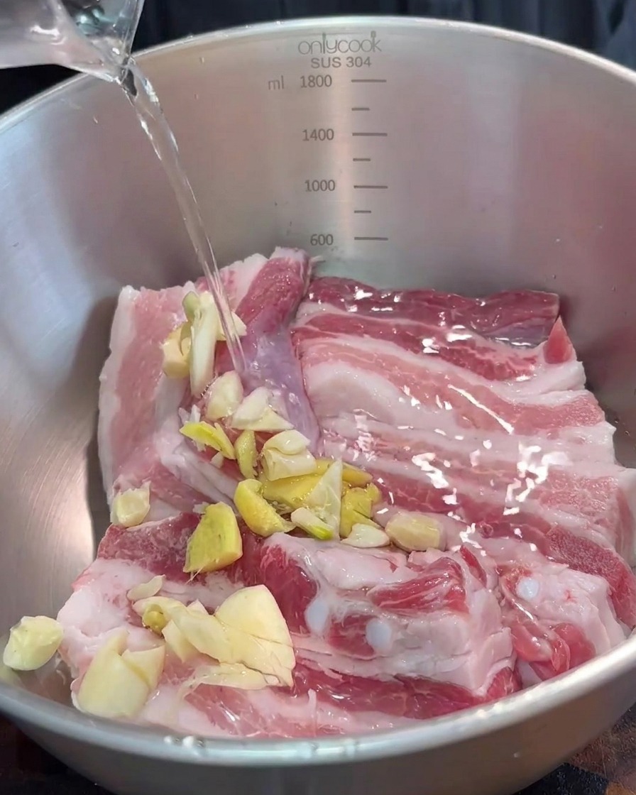 Un bol contenant les lanières de porc assaisonnées avec des aromates hachés et de la sauce au tofu rouge fermenté.