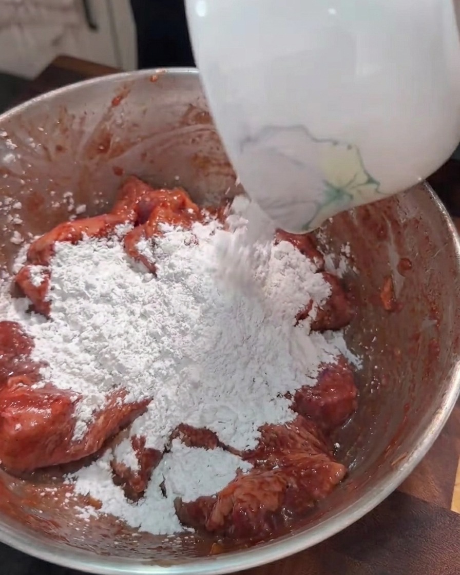 Fécule de patate douce versée dans un bol de lanières de porc marinées.