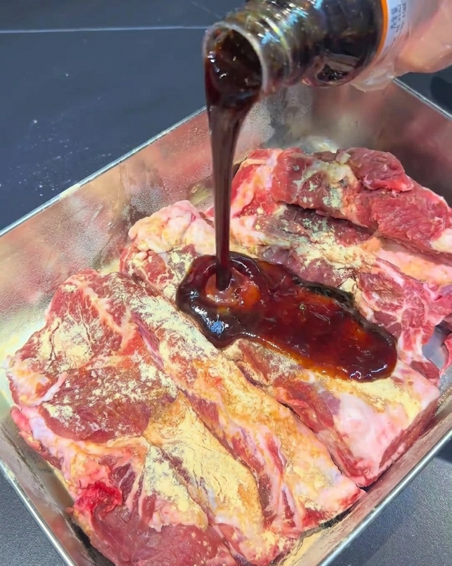 Sauce marinade sombre versée dune bouteille en verre sur des travers de porc assaisonnés dans un plateau en métal.