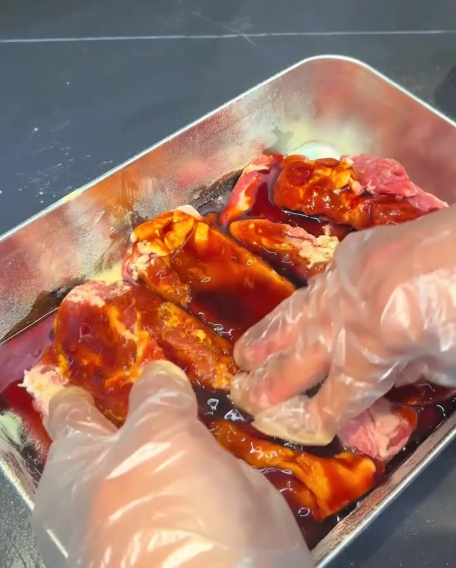 Travers de porc massés et enrobés dune sauce marinade sombre dans un récipient en métal.