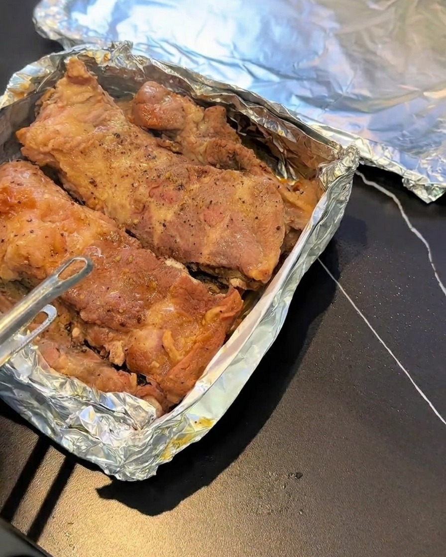 Travers de porc cuits à la vapeur reposant sur une plaque de cuisson recouverte de papier daluminium, assaisonnés de poivre noir.