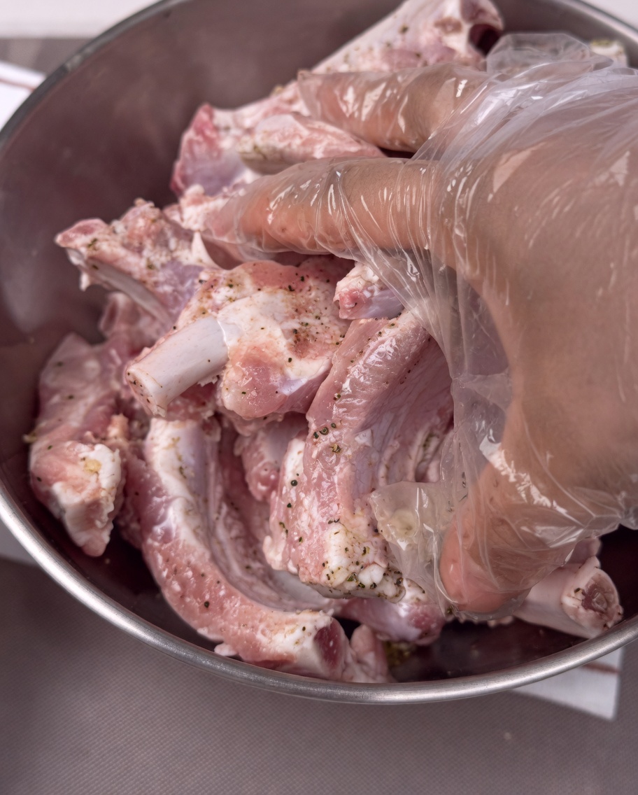 Mains gantées mélangeant les travers de porc dans un bol en acier inoxydable.