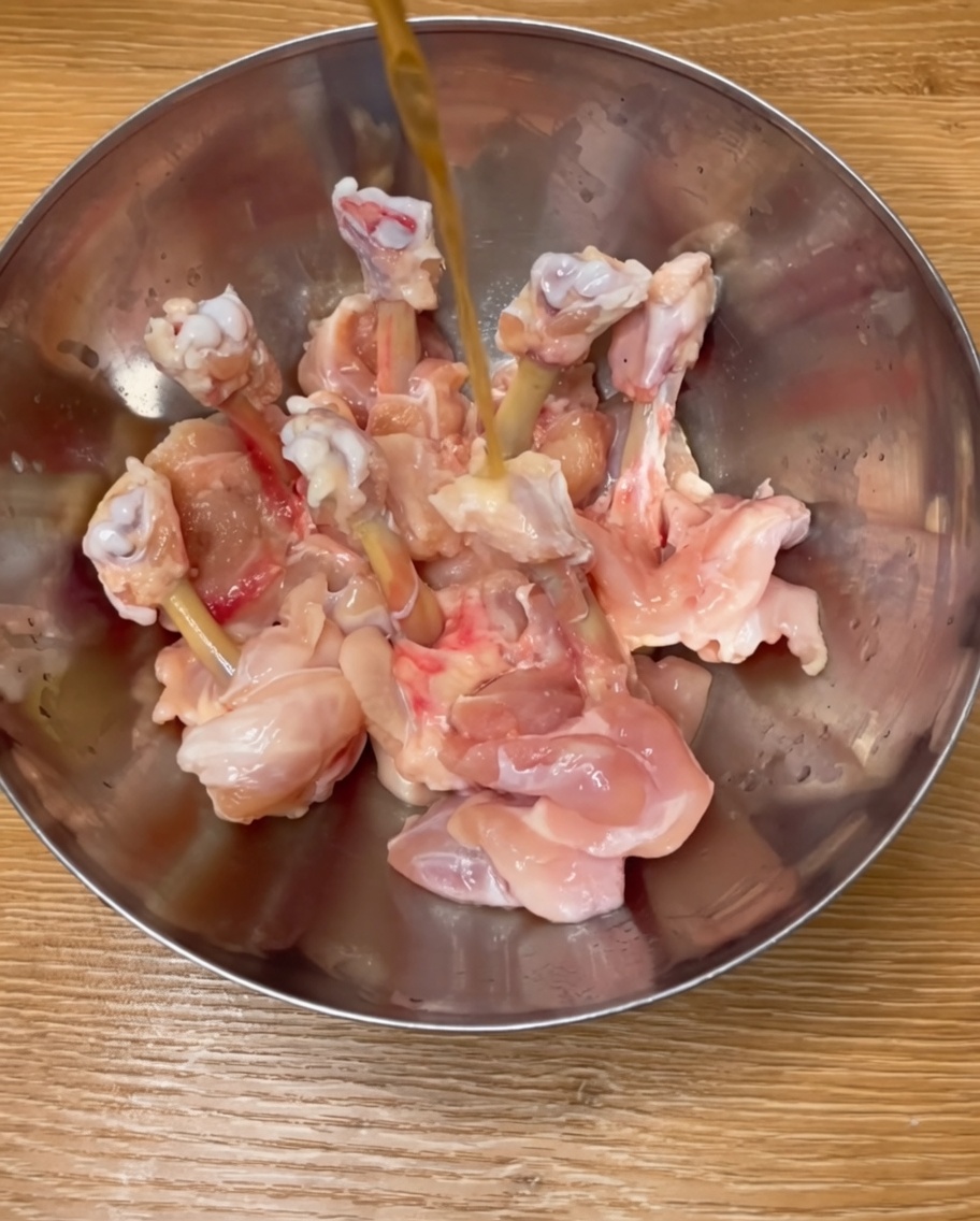 Pilons de poulet assaisonnés dans un bol en métal avec du vin de riz, des épices et lœuf battu.