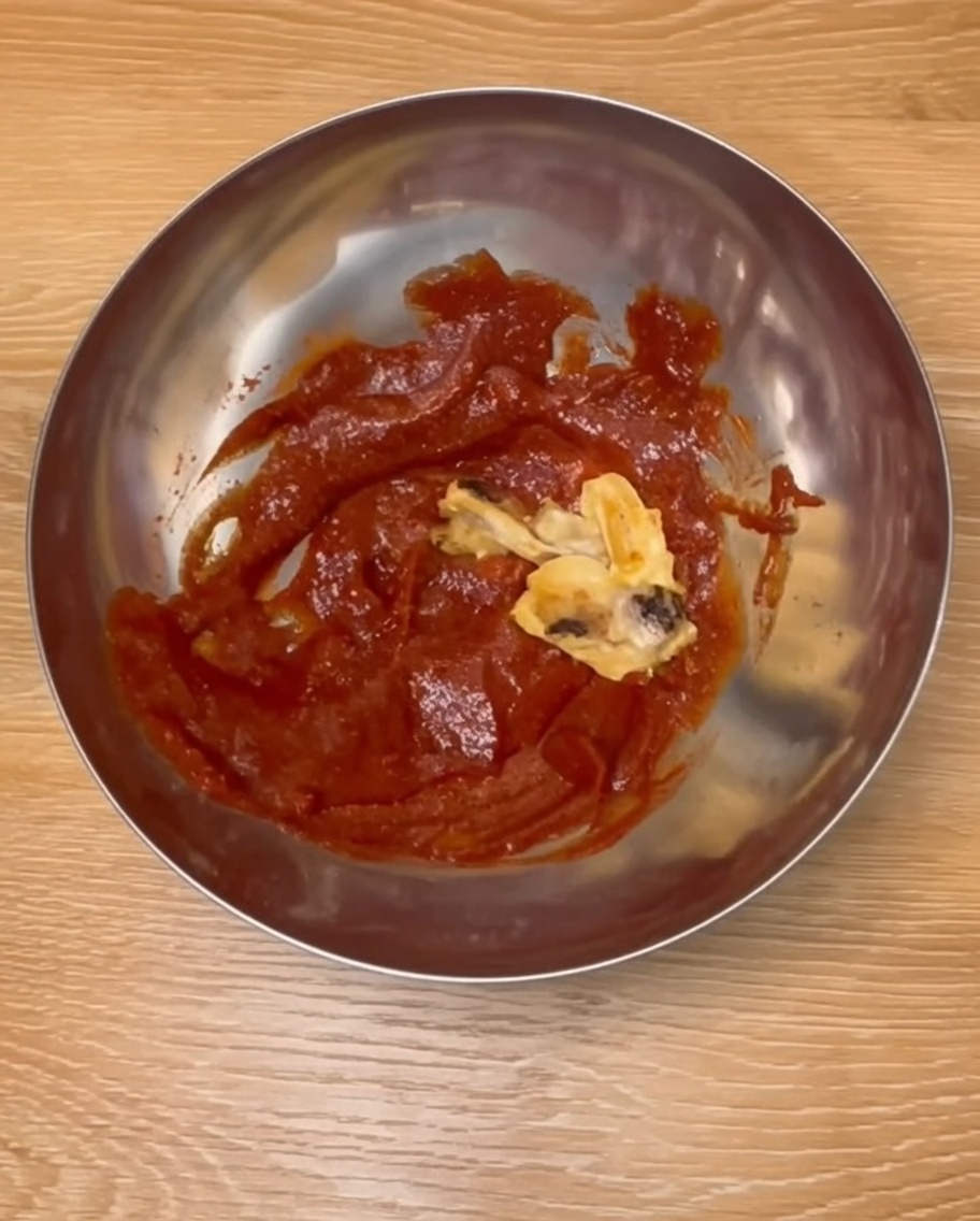 Pilons de poulet cuits mélangés avec une sauce coréenne rouge riche dans un bol en inox.