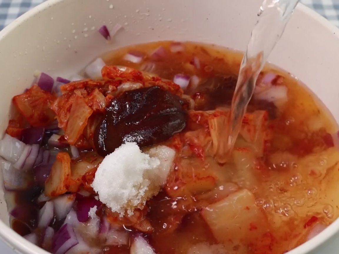 Eau versée dans la marmite avec la base de kimchi et dassaisonnements.
