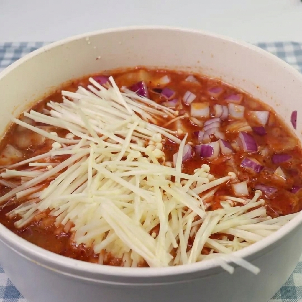 Champignons enoki et morceaux de spam ajoutés dans la soupe au kimchi frémissante.