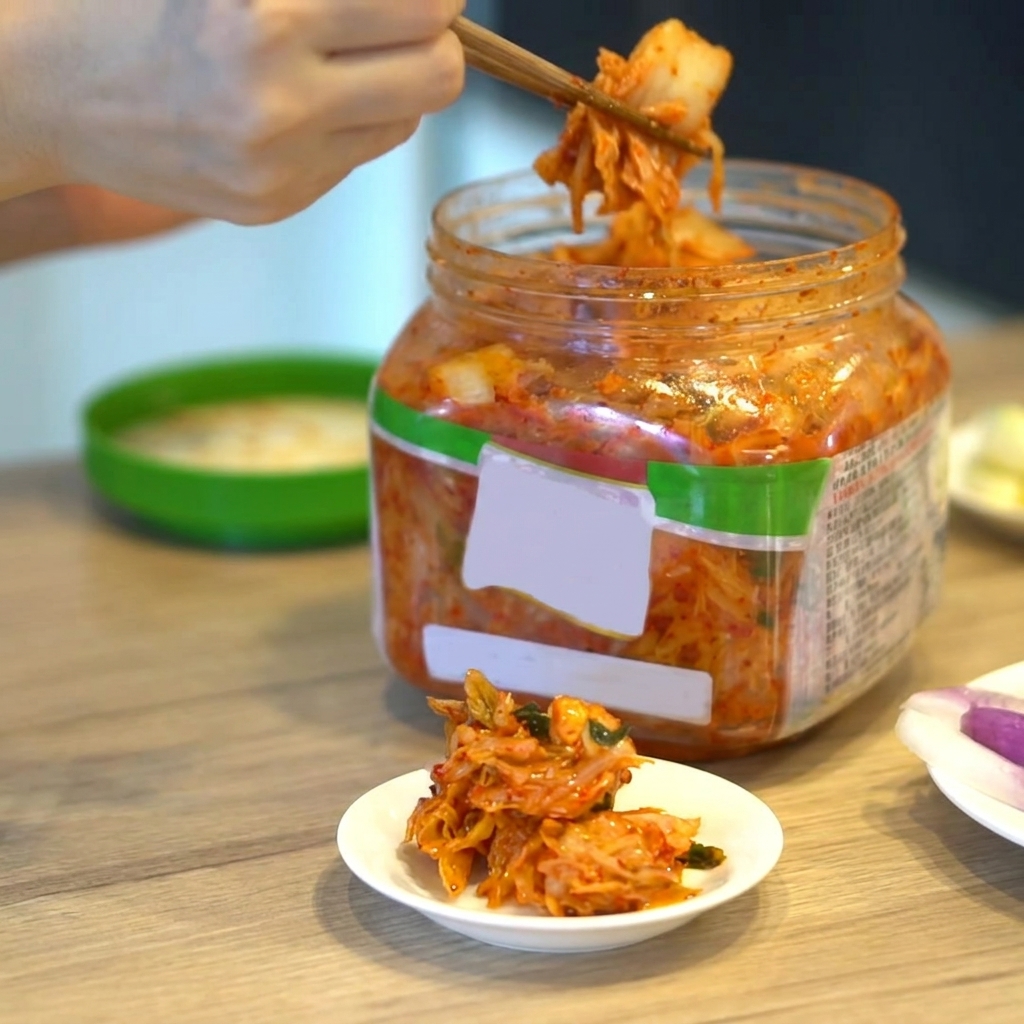 Une portion de kimchi coréen soulevée dun récipient avec des baguettes.