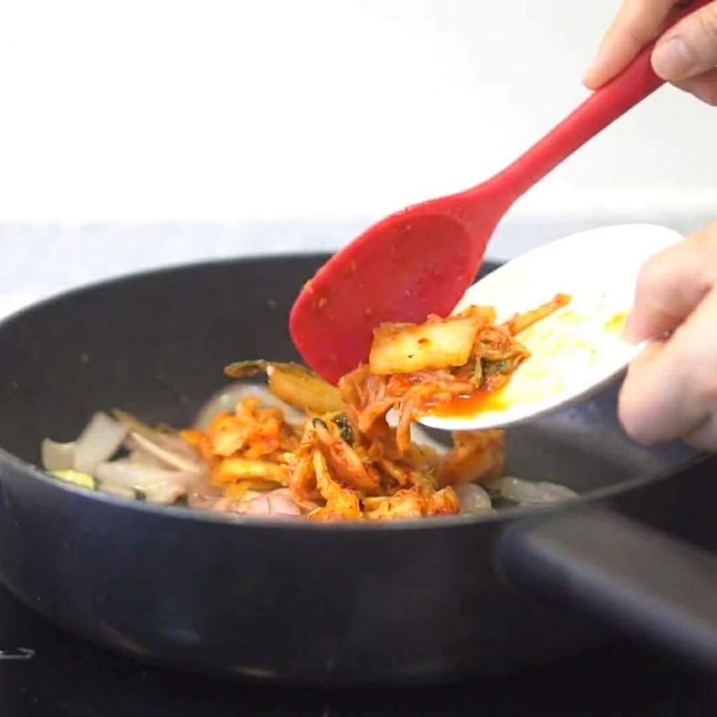 Kimchi ajouté dans une poêle avec les oignons et lail sautés.