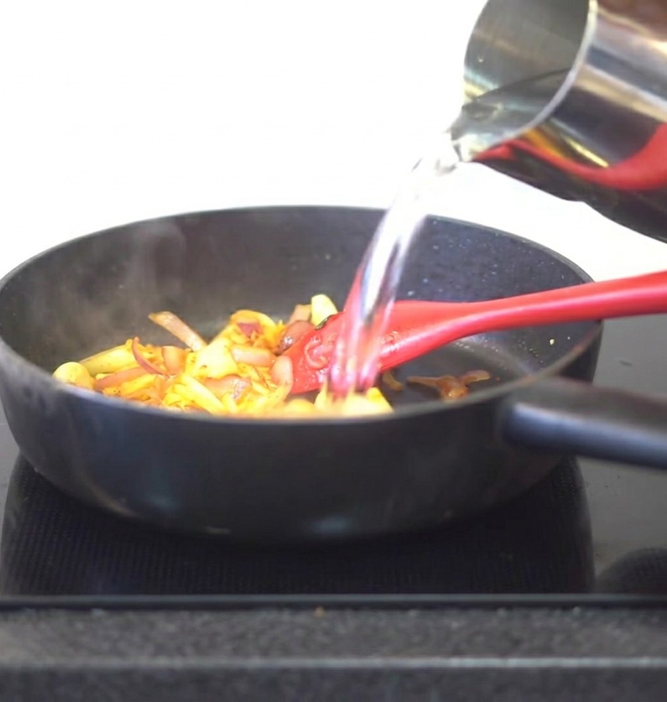 Eau versée depuis une carafe en métal dans une poêle contenant le kimchi et les aromates sautés.