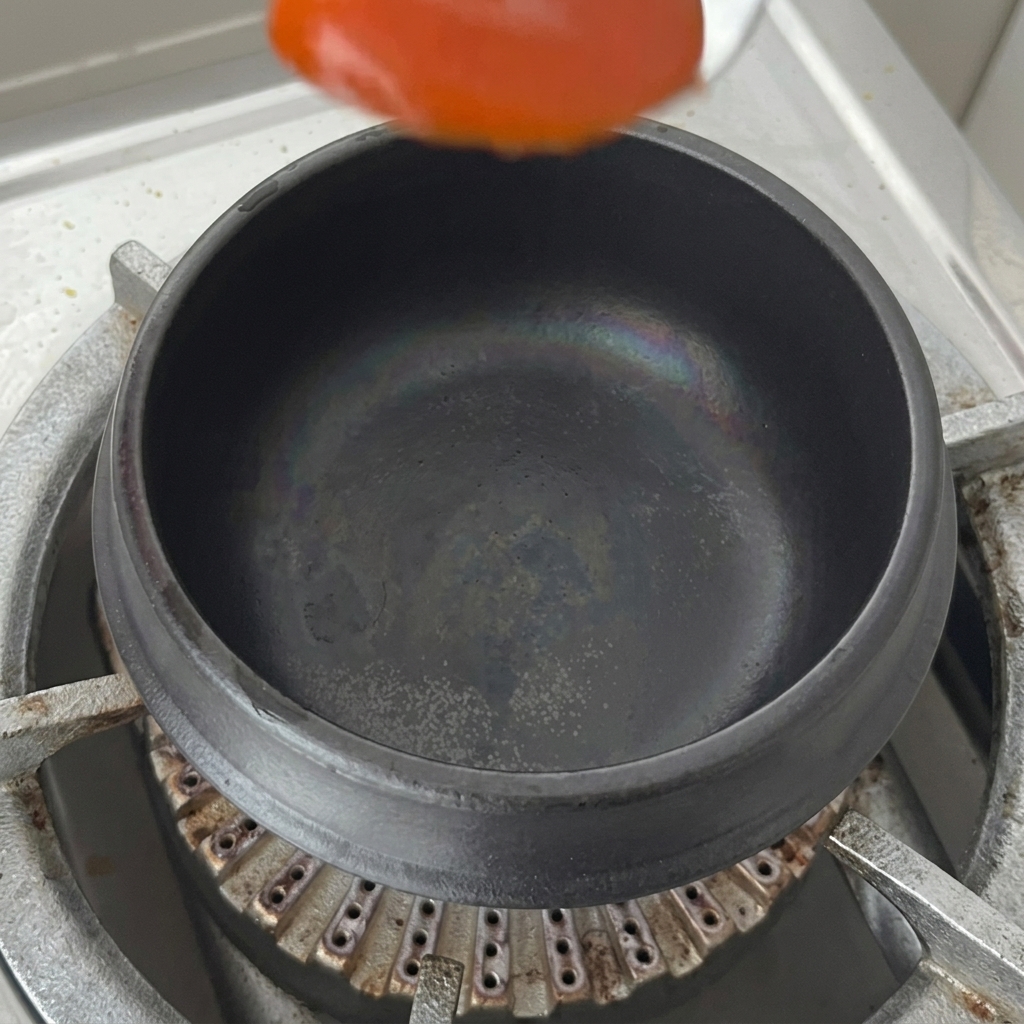 Une cuillère de sauce au piment rouge déposée au fond dun pot en terre cuite sec sur la cuisinière.