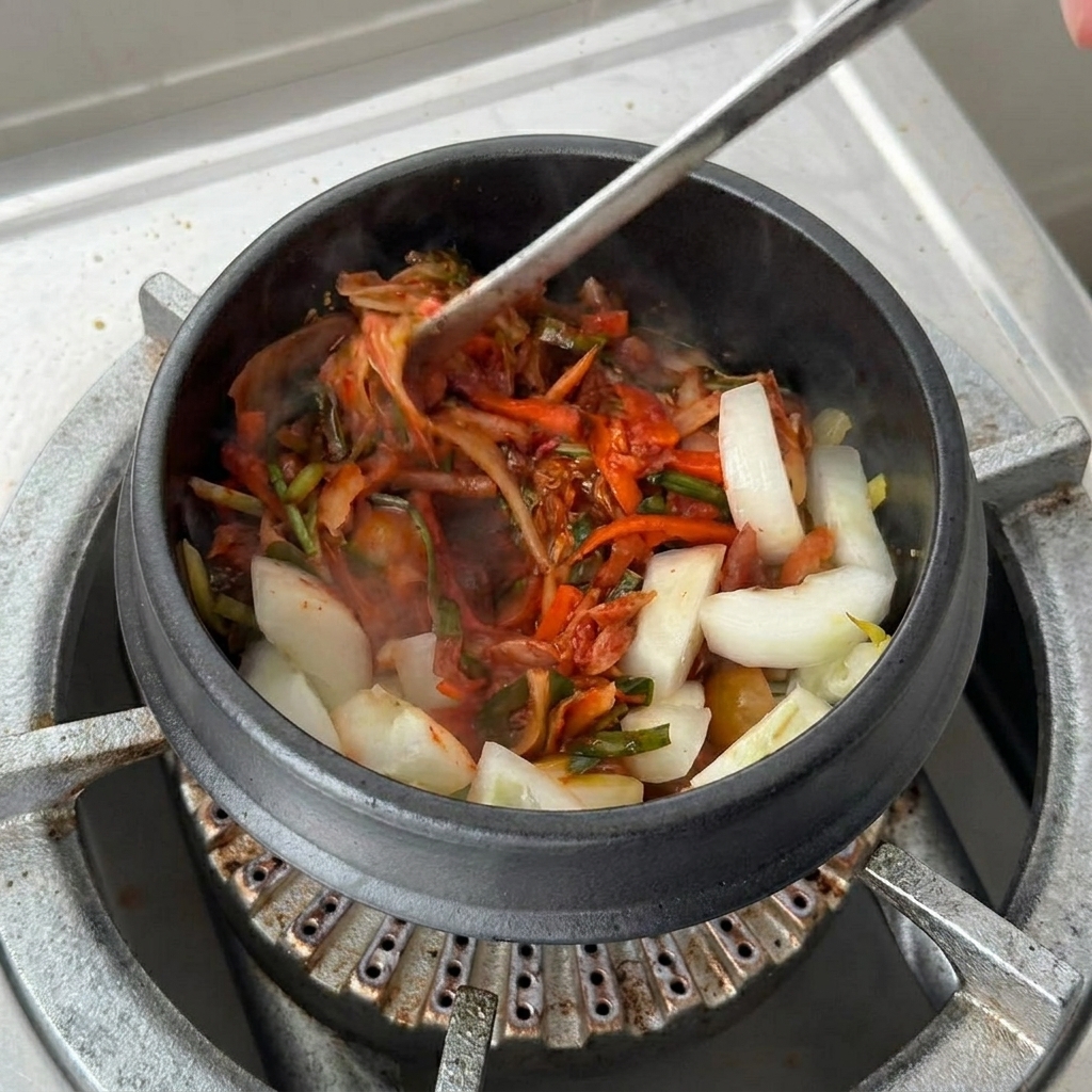 Une tasse de jus de kimchi versée dans le pot en terre cuite sur le kimchi et les oignons sautés.